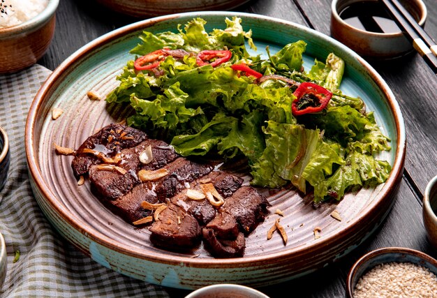 Seitenansicht von gebratenem Rindfleisch mit Salat und rotem Chili auf einem Teller auf Holz