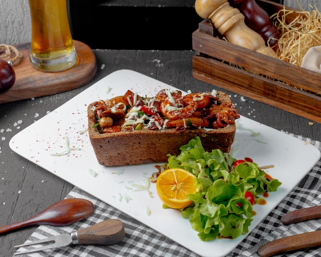 Seitenansicht von gebratenem Tintenfisch und Tintenfisch mit Käse und Kartoffeln ua ein hinterlegtes Brot