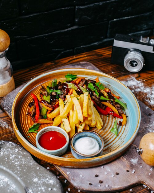 Seitenansicht von gegrilltem Rindfleisch mit Gemüse, das mit Pommes Frites und Saucen auf Teller serviert wird