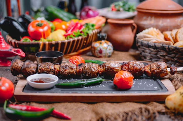 Seitenansicht von gegrillten Kartoffeln auf Schaschlik, serviert mit Gemüse und Saucen auf einem Holzbrett