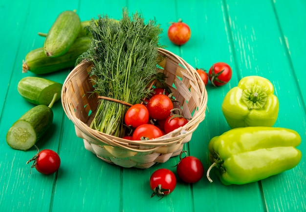 Seitenansicht von Gemüse als Bündel von Dill und Tomaten im Korb mit geschnittenen Gurkenpaprika und Tomaten auf Grün