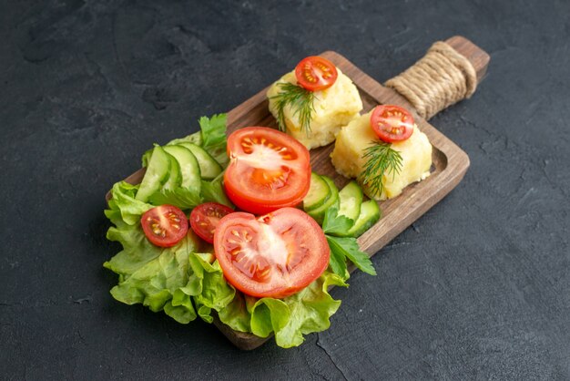 Seitenansicht von geschnittenem frischem Tomaten- und Gurkenkäse auf Holzbrett auf schwarzer Oberfläche