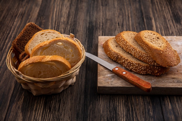 Seitenansicht von geschnittenen Broten brauner Samenkolben mit Messer auf Schneidebrett und Roggenweiß im Korb auf Holzhintergrund