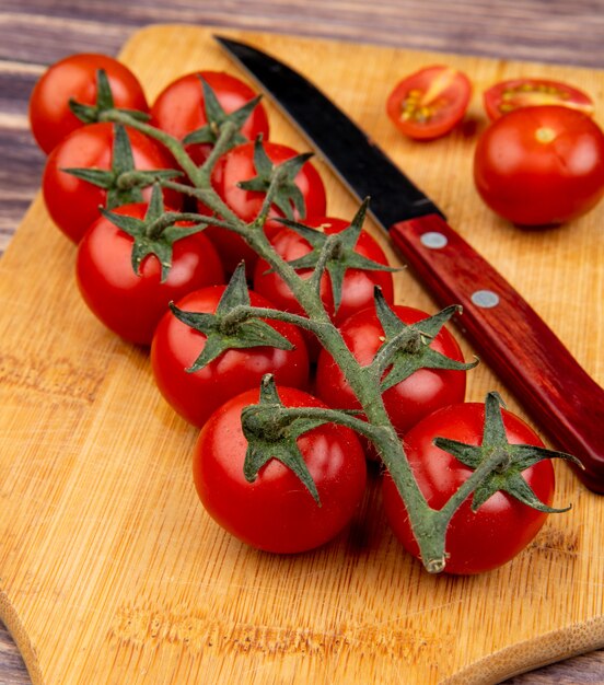 Seitenansicht von geschnittenen und ganzen Tomaten mit Messer auf Schneidebrett auf Holztisch