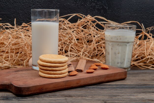 Seitenansicht von Glas Milch und Keksen Mandeln auf Schneidebrett auf Holzoberfläche und schwarzer Wand