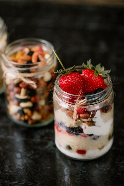 Seitenansicht von Hafer über Nacht mit frischen Erdbeeren, Blaubeeren und Nüssen in einem Glas auf dunkler Oberfläche