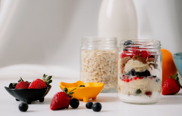 Seitenansicht von Hafer über Nacht mit frischen Erdbeeren, Blaubeeren und Nüssen in einem Glas auf rustikalem Tisch