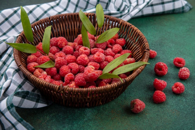 Seitenansicht von Himbeeren mit Blättern im Korb auf kariertem Stoff und Grün