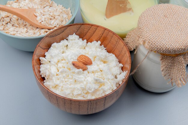 Seitenansicht von Hüttenkäse in Schüssel mit Mandeln und Haferflocken Kondensmilchcreme auf blauem Tisch