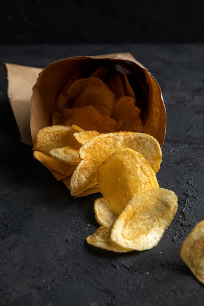 Kostenloses Foto seitenansicht von kartoffelchips, die von einem pfeffersack auf schwarz verstreut sind