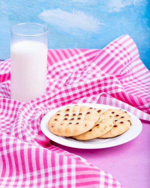 Seitenansicht von Keksen auf einem weißen Teller serviert mit einem Glas Milch auf rosa