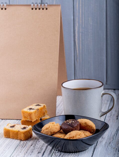 Seitenansicht von Keksen in einer schwarzen Schüssel und einer Tasse mit Kakao auf Holz