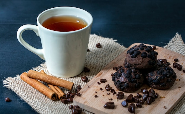 Seitenansicht von Keksen und Schokolade auf Schneidebrett mit Tasse Tee und Zimt auf Sackleinen und blauem Hintergrund