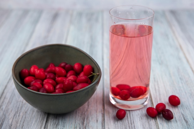 Seitenansicht von Kornelkirschenbeeren in Schüssel und Kornelkirtensaft in Glas auf hölzernem Hintergrund