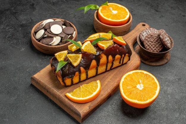 Seitenansicht von leckeren Kuchen schneiden Orangen mit Keksen auf Schneidebrett auf dunklem Tisch