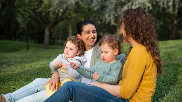 Seitenansicht von lgbt müttern draußen im park mit ihren kindern, die sich auf gras entspannen