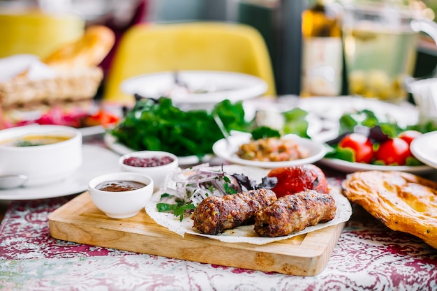 Seitenansicht von Lula Kebab auf Lavash mit gegrillten frischen Tomatenkräutern und Gewürzen auf einem Holzbrett