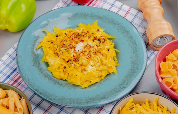 Seitenansicht von Makkaroni-Nudeln in Teller mit verschiedenen Makkaronis als Tagliatelle und anderen mit Salzpfeffer auf kariertem Stoff