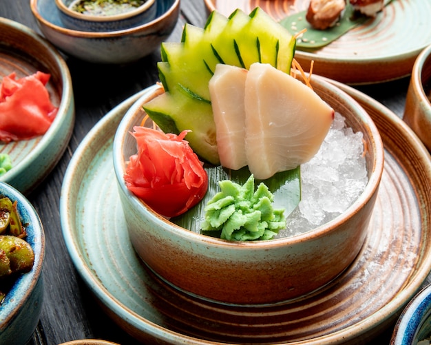 Seitenansicht von marinierten Heringsfilets mit geschnittenem Gurken-Ingwer und Wasabi-Sauce auf Eiswürfeln in einem Teller auf dem Tisch