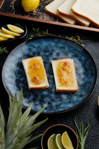 Seitenansicht von mit Marmelade bestrichenen Brotscheiben mit Zitrusfrüchten als Ananas-Kiwi-Orangen-Limetten-Zitronen- und Mandarinenscheiben mit Zitronenbrotscheiben in einem Tablett auf schwarzem Hintergrund