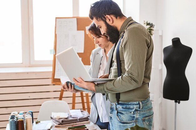 Seitenansicht von Modedesignern, die im Atelier mit Laptop arbeiten