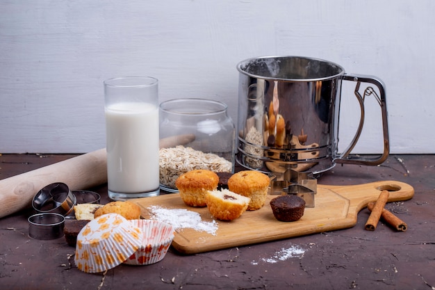 Seitenansicht von Muffins und einem Glas Milch auf einem hölzernen Schneidebrett