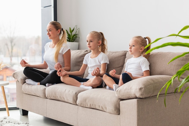 Seitenansicht von Mutter und Töchtern, die zu Hause auf der Couch meditieren