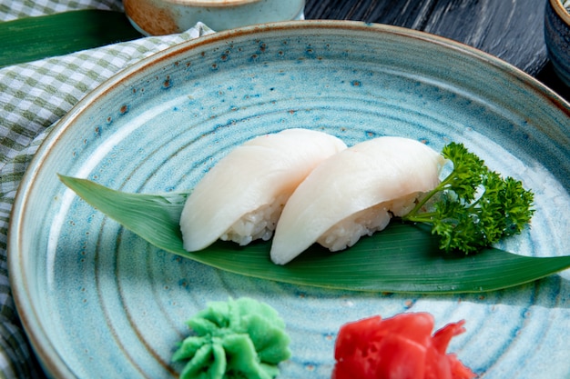 Seitenansicht von Nigiri-Sushi auf Bambusblatt, serviert mit eingelegten Ingwerscheiben und Wasabi auf einem Teller