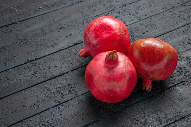 Seitenansicht von oben aus der Ferne drei Granatäpfel drei reife Granatäpfel auf dunklem Tisch