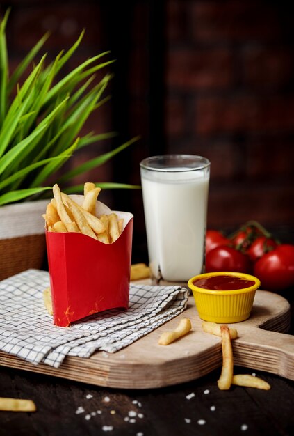 Seitenansicht von Pommes Frites in Pappbeutel mit Ketchup auf Holzschneidebrett