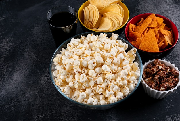 Seitenansicht von Popcorn und Pommes in Schalen auf schwarzer horizontaler