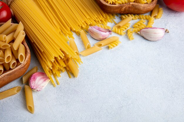 Seitenansicht von rohen Spaghetti mit rohen Nudeln in Schalen mit Knoblauch auf einer grauen Oberfläche