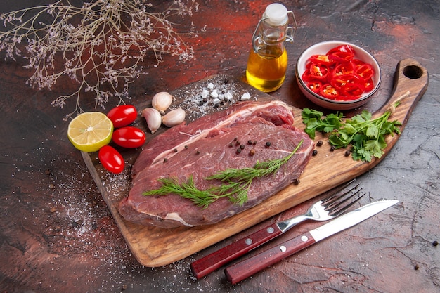 Seitenansicht von rotem Fleisch auf Holzbrett und Knoblauch-grüne Zitrone gehackte Paprika-Tomatenölflasche auf dunklem Hintergrund