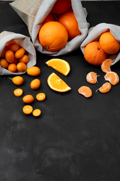 Seitenansicht von Säcken voller Zitrusfrüchte als Orangen-Mandarinen-Kumquat auf schwarzer Oberfläche