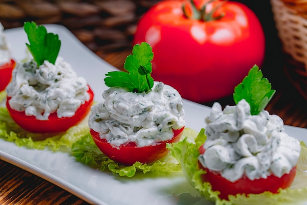 Seitenansicht von Sauerrahmjoghurt mit Gurken galic und Kräutern auf frischen Tomaten gekrönt mit Petersilie auf einem Teller