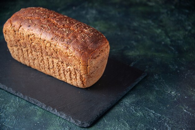 Seitenansicht von Schwarzbrot auf schwarzem Brett auf gemischtem, beunruhigtem Hintergrund