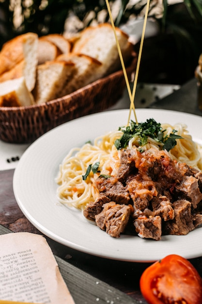 Seitenansicht von Spaghetti mit Fleischstücken und Tomaten auf einem Holzbrett