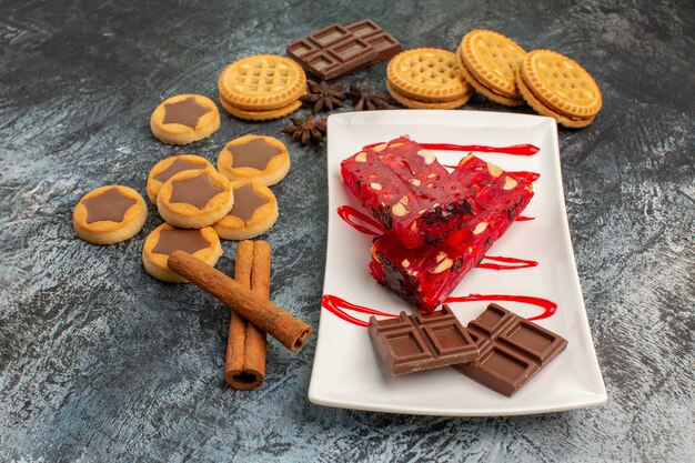 Seitenansicht von süßer Schokolade auf weißem Teller mit Keksen und Zimtstangen auf grauem Grund