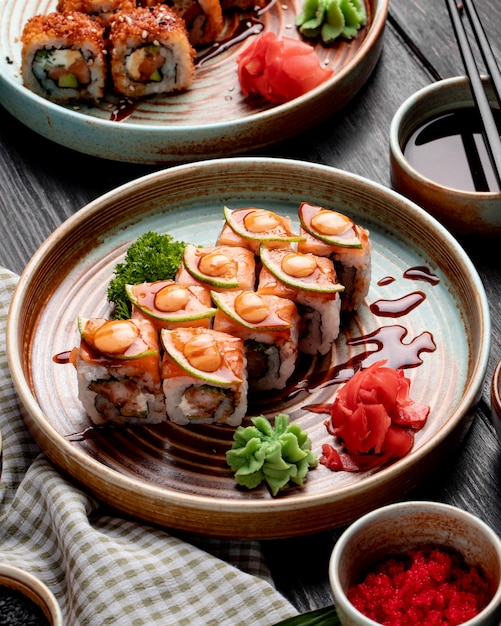 Seitenansicht von Sushi-Rollen mit Garnelen-Avocado und Frischkäse, serviert mit Ingwer und Wasabi auf einem Teller auf Holz
