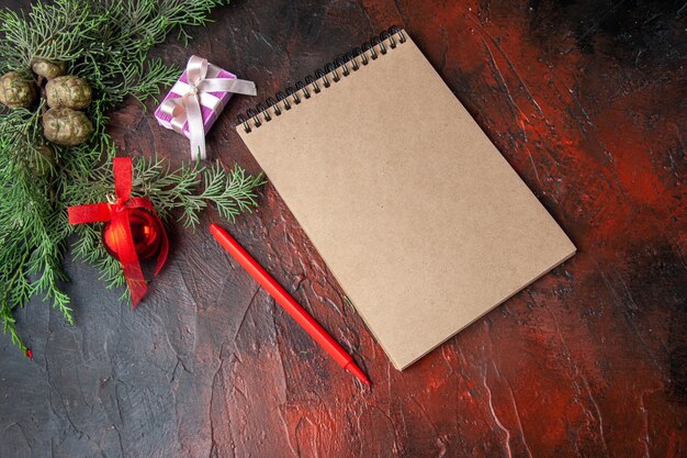 Seitenansicht von Tannenzweigen mit Dekorationszubehör und Geschenk neben Notebook auf dunklem Hintergrund