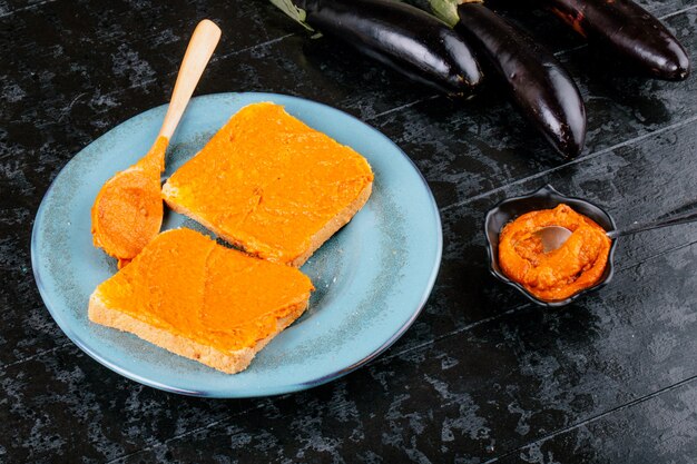 Seitenansicht von Toast mit Auberginenkaviar auf einem blauen Teller auf schwarzem Holztisch