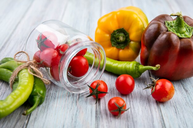 Seitenansicht von Tomaten, die aus Glas mit Paprika auf Holz verschütten