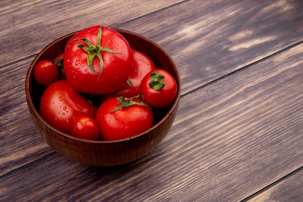 Seitenansicht von Tomaten in der Schüssel auf der linken Seite und Holztisch mit Kopierraum