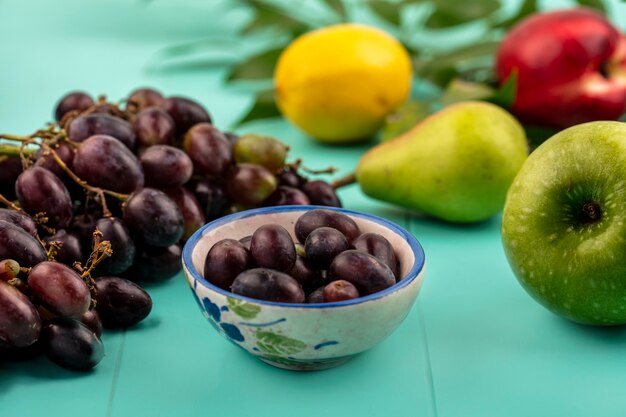 Seitenansicht von Traubenbeeren in Schüssel und Traubenapfel mit Birnenpfirsichzitrone auf blauem Hintergrund