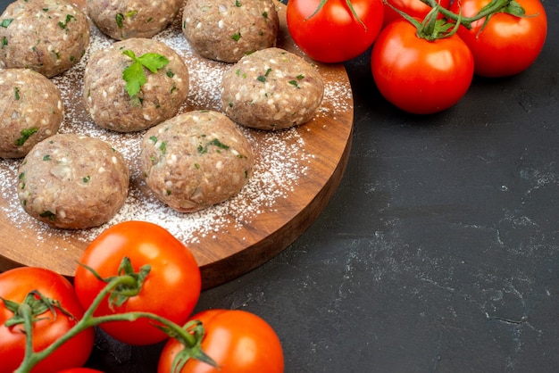 Seitenansicht von ungekochten Fleischbällchen mit Grün in einem braunen Teller und Tomaten mit Stielen auf schwarzem Hintergrund mit freiem Platz