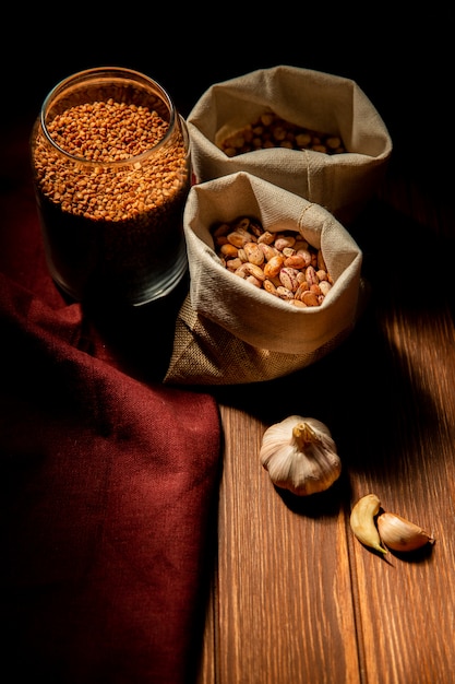 Seitenansicht von verschiedenen Arten von Hülsenfrüchten und Getreide Kidneybohnen Buchweizen und Kichererbsen in Säcken auf dunklem Tisch