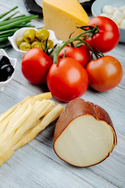 Seitenansicht von verschiedenen Käsesorten mit frischen Tomaten und eingelegten Oliven auf grauem Holztisch