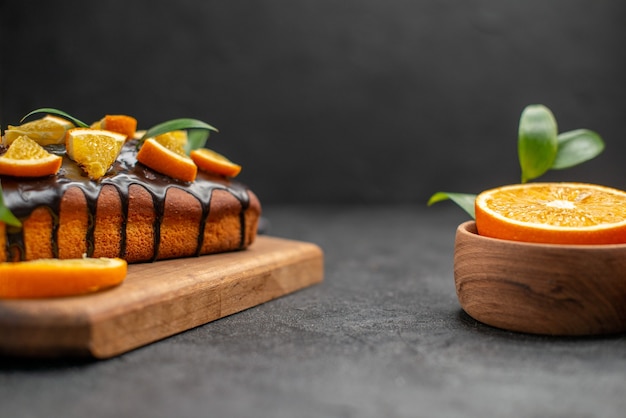 Seitenansicht von weichen Kuchen und geschnittenen Orangen mit Blättern auf dunklem Tisch