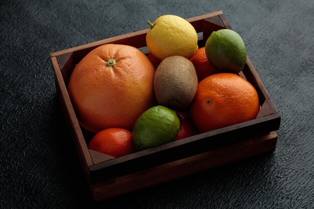 Seitenansicht von Zitrusfrüchten als Orangen-Kiwi-Limetten-Zitronen-Mandarine in Box auf schwarzem Hintergrund