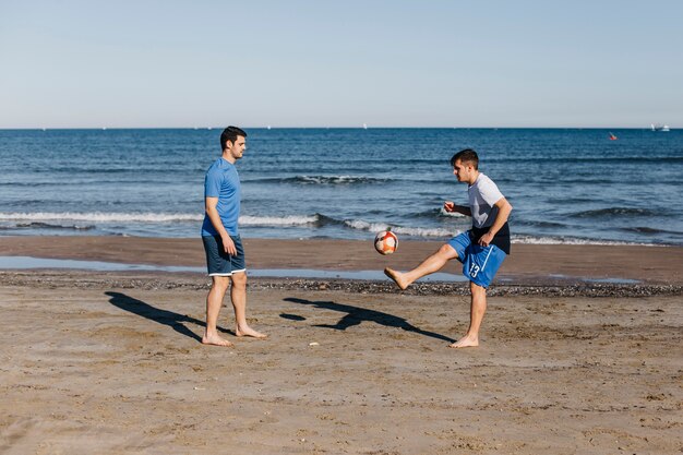 Seitenansicht von zwei Freunden, die Fußball am Strand spielen